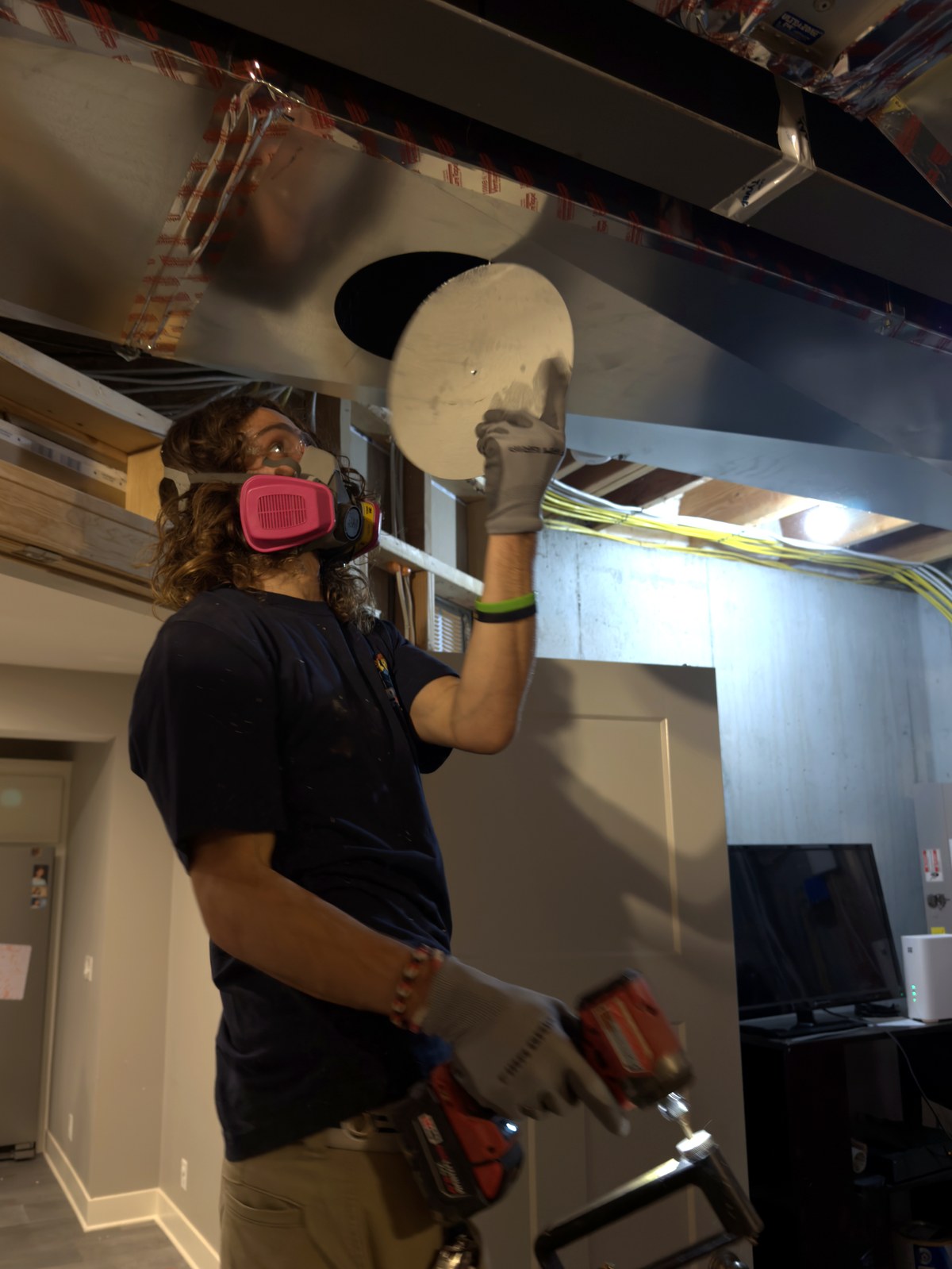 A Duct Daddy technician in a company shirt and respirator capping a service access on a main trunk line in a Kansas City home